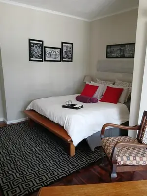 a bedroom with a bed with red pillows and a chair at Rusticana Room1 in Cape Town
