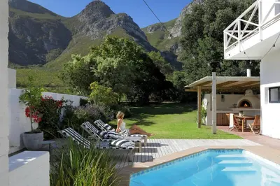 a woman sitting in chairs next to a swimming pool at Best of Both! Mountain and Sea View Home. in Hermanus