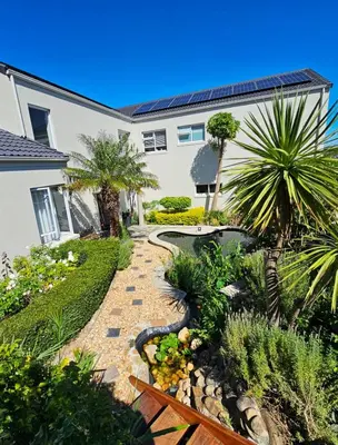 a garden in front of a house with palm trees at Casa La Vista in Somerset West