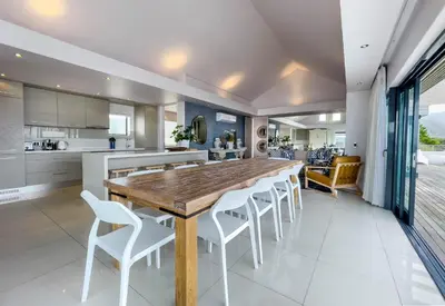 a kitchen and dining room with a wooden table and white chairs at Le Paradis Penthouse in Hermanus