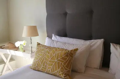 a bed with white pillows and a table with a lamp at The Cottage on 55 in Franschhoek