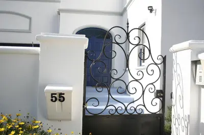 a gate to a white house with a blue door at The Cottage on 55 in Franschhoek