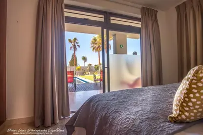 a bedroom with a bed and a sliding glass door at Sunset Beach Luxury Apartments in Cape Town