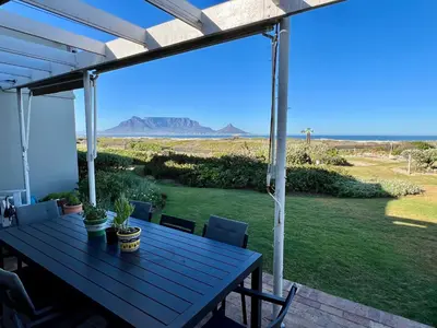 a picnic table on a porch with a view of the desert at 4-Bedroom cabana at Dolphin Beach in Cape Town