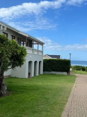 a white house with a grass yard next to the ocean at True coastal living - 2gether on Voëlklip in Hermanus