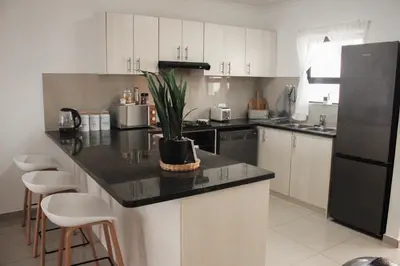 a kitchen with white cabinets and a black refrigerator at Modern 2 bedroom apartment close to shops & beach in Gordonʼs Bay