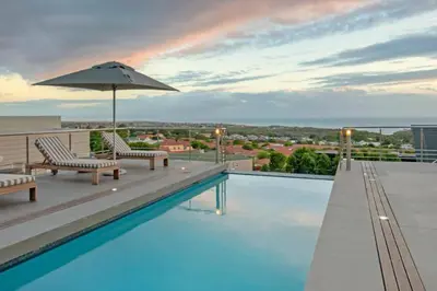 a swimming pool with chairs and an umbrella on a roof at Waterstone Villa in Hermanus