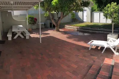 a patio with two white benches and an umbrella at House in Hermanus Voëlklip in Hermanus