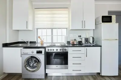 a white kitchen with a washer and a dishwasher at The Rondebosch Views in Cape Town
