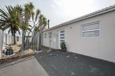 a white building with palm trees and a fence at WiFi & Solar at Studio on Morgenster in Cape Town