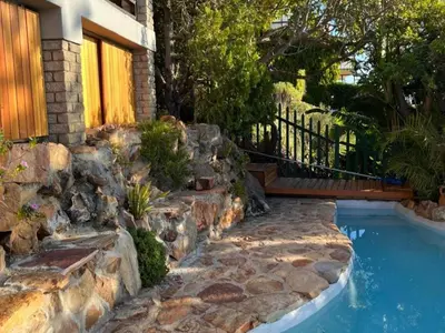 a swimming pool with a rock retaining wall and a house at Artists Cottages Gordon's Bay in Cape Town