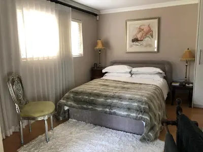 a bedroom with a bed and a chair and a window at Dusk 2 Dawn Self Catering Guest House in Cape Town