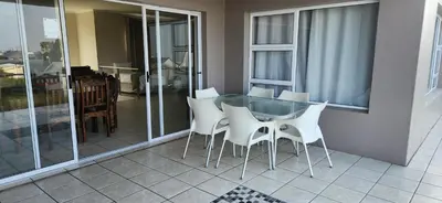 a dining room with a glass table and white chairs at Picollo Bocca Villa Kleinmond in Kleinmond