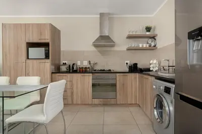 a kitchen with wooden cabinets and a table and white chairs at Mayfair Apartments in Cape Town