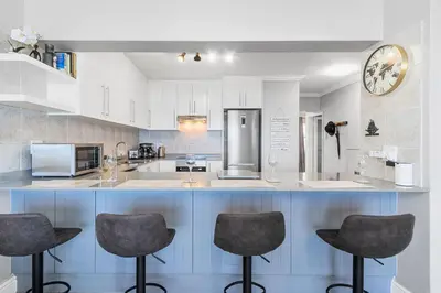 a kitchen with three bar stools and a clock on the wall at 9 On The Waves in Cape Town