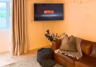 a living room with a couch and a television on the wall at Silvertree Collective Spacious Central Apartment in Stellenbosch