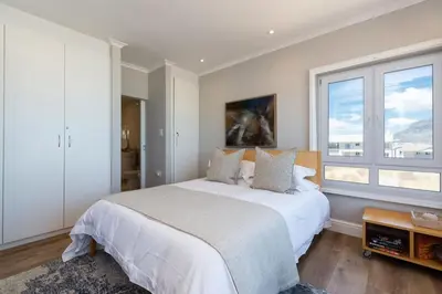 a bedroom with a large bed and two windows at Lagoon Beach Penthouse in Cape Town