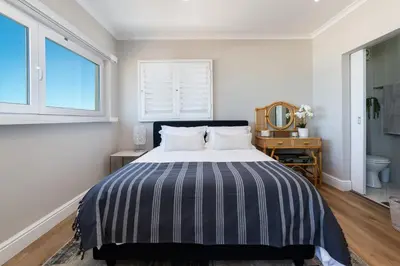 a bedroom with a bed with a striped comforter and a mirror at Lagoon Beach Penthouse in Cape Town