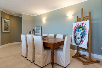 a dining room with a wooden table and white chairs at Lagoon Beach Penthouse in Cape Town