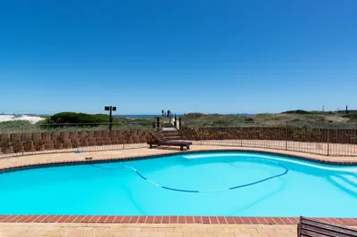 a large blue swimming pool with a bench in front of a fence at Lagoon Beach Penthouse in Cape Town