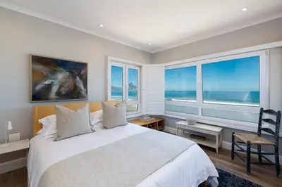 a bedroom with a large bed and large windows at Lagoon Beach Penthouse in Cape Town