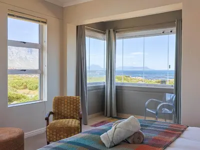 a child laying on a bed in a bedroom with windows at Penguin View in Bettyʼs Bay