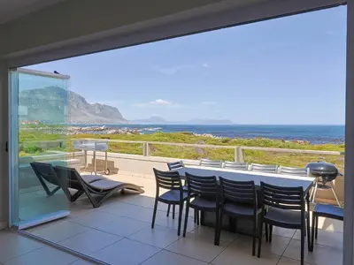 a balcony with a table and chairs and the ocean at Penguin View in Bettyʼs Bay