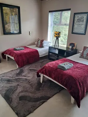 a bedroom with two beds with red blankets and a rug at Listening Wind Self-Catering accommodation in Bettyʼs Bay