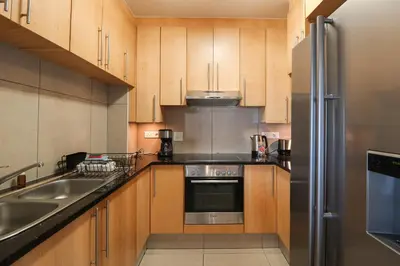 a kitchen with wooden cabinets and a stainless steel refrigerator at 1402 Hibernian Towers Luxury Self Catering Apartment Strand Western Cape South Africa in Cape Town