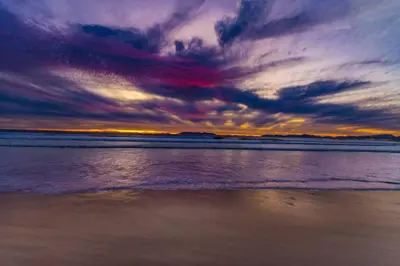 a sunset on the beach with a cloudy sky at Elegance on Beach in Cape Town