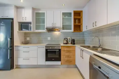 a kitchen with white cabinets and a stainless steel refrigerator at Chic, Cozy, Modern, Secure and Centrally Located in Cape Town
