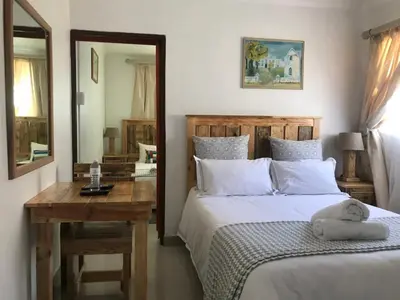 a bedroom with a bed and a desk and a mirror at MELJAA GROUP Guesthouse in Cape Town