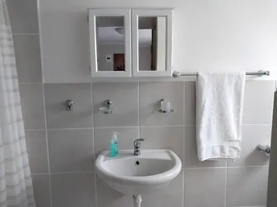a white bathroom with a sink and a cabinet at Neptune in Gordonʼs Bay