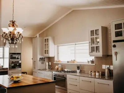 a kitchen with white cabinets and a table and a chandelier at Cape Select Luxury Accommodation in Durbanville