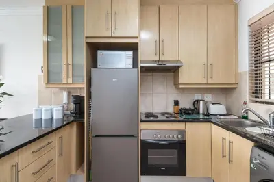 a kitchen with wooden cabinets and a white refrigerator at Spacious 1 Bedroom Flat Church St Stellenbosch in Stellenbosch