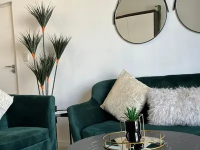 a living room with two green chairs and a circular mirror at Luxury Stays in Cape Town