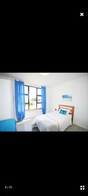 a bedroom with two beds and a window with blue curtains at Sea View Room in Gordonʼs Bay