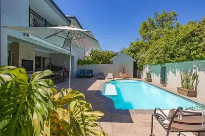 a swimming pool with chairs and an umbrella next to a house at Luxury Five Bed House in the Heart of Franschhoek in Franschhoek