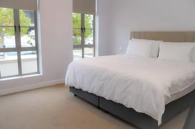a bedroom with a bed with white sheets and windows at 24 Le Bourgette in Franschhoek