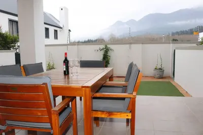 a wooden table with chairs and a bottle of wine at 24 Le Bourgette in Franschhoek
