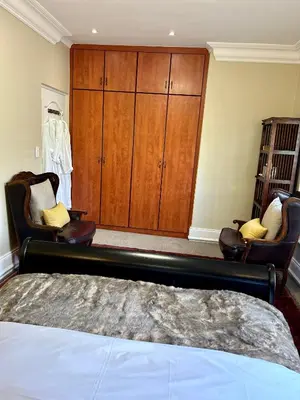 a bedroom with a bed and two chairs and a cabinet at French Manor 2 Stellenbosch in Stellenbosch