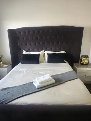 a bed with a black headboard and two towels on it at Spacious Double Room with Pool, Free WiFi, Self-Catering Kitchen in Cape Town