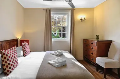a bedroom with a bed with a chair and a window at Bo La Motte Farm Cottages in Franschhoek