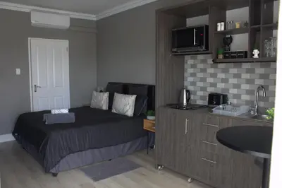 a small bedroom with a bed and a kitchen at Charming Modern Bedsitter in Cape Town