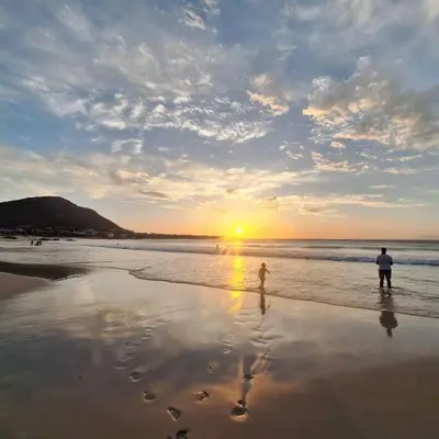 a couple of people standing on the beach at sunset at Beautiful family beach cottage! in Pringle Bay