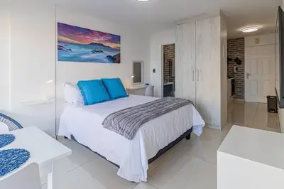 a white bedroom with a large bed with blue pillows at Beach Front Sea View Apartment, Table View in Cape Town