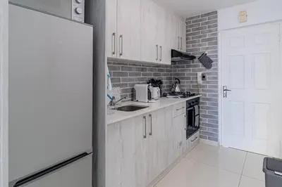 a kitchen with white cabinets and a brick wall at Beach Front Sea View Apartment, Table View in Cape Town