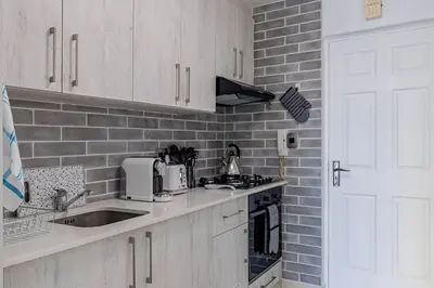 a kitchen with white cabinets and a brick wall at Beach Front Sea View Apartment, Table View in Cape Town