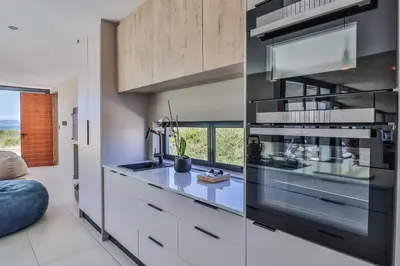 a kitchen with white cabinets and a counter with a window at The Dunes in Bettyʼs Bay