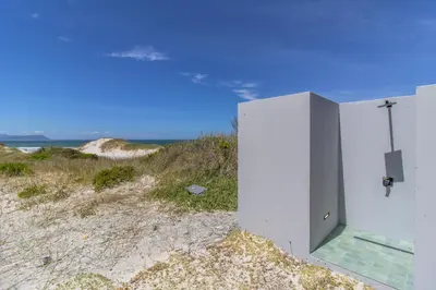 a white building on the beach with the ocean in the background at The Dunes in Bettyʼs Bay